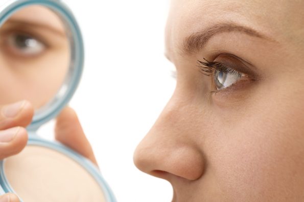 Close-up of woman with nicely shaped nose, looking in compact mirror.